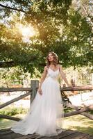 beautiful girl in white dress with a wreath of flowers on her head is standing outdoor in the park with green leaf on the background photo