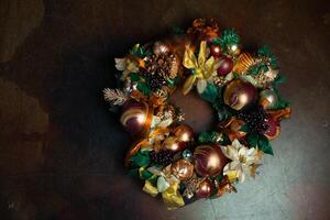 Christmas wreath on brown background with copyspace. Wreath decorated with balls and bows of gold and brown, with green leaves photo