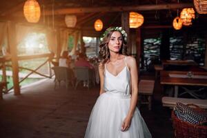 the bride in a white dress and a wreath of flowers is in the restaurant photo