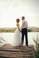 Boda Pareja caminando en puente cerca lago en puesta de sol a Boda día. novia y novio en amor foto