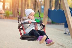 Happy child girl on swing in sunset fall. Little kid playing in the autumn on the nature park photo