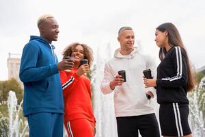 Group of young people of different nationalities in sportswear are drinking coffee and chatting. Two men and two women. Healthy lifestyle. photo
