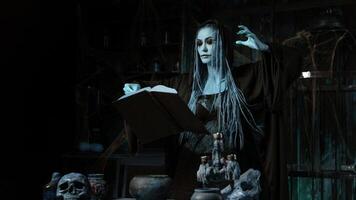 Halloween concept. Witch dressed black hood with dreadlocks standing dark dungeon room use magic book for conjuring magic spell photo