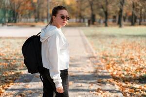 un joven hermosa mujer con un cola de caballo y Gafas de sol, con un mochila en su espalda en el parque. foto desde el espalda