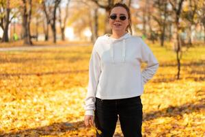 Portrait of beautiful young woman in a white sweater and sunglasses walking outdoors in autumn photo