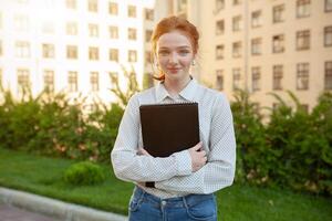 Beautiful red haired girl with freckles hugging notebooks with homework and smiling happy. Back to school concept. Portrait of a student photo