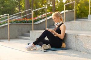 Sport and Fitness Young Adult Caucasian Woman Sitting Exercise Mat Concrete Floor Resting after morning Workout Outdoor Summer Park photo