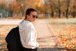 A young beautiful woman with a ponytail and sunglasses, with a backpack on his shoulders in the park. Photo from the back