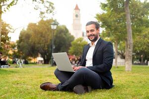 Handsome hispanic male businessman sitting lotus position in public park use laptop photo