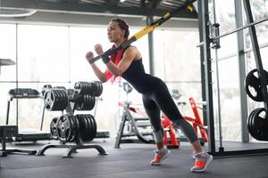 Athlete woman training exercising with suspension system indoor gym. Beautiful caucasian sportive woman do stretching strenght exercise with special strap photo