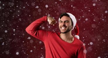 Young handsome caucasian guy in a red sweater and Santa hats stands on red background in studio and showing biceps power photo