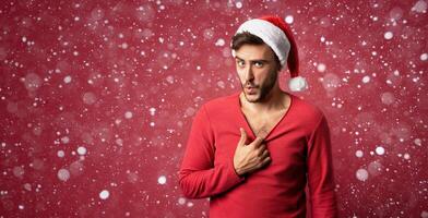 Young handsome caucasian guy in red sweater and Santa hats stands on red background in studio and Shows how hot he is photo