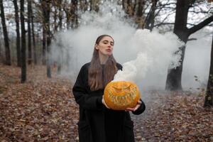 Young woman holding the halloween pumpkin with the white smoke coming from inside of it photo