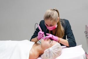 cosmetología gabinete cliente mentiras en sofá. cosmetólogo aplica calificación en Cejas. foto