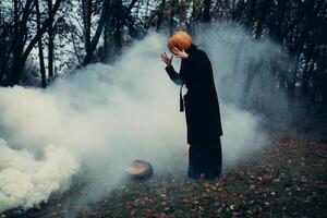 A man in a long black coat with a pumpkin instead of a head in a terrible night forest, damp and fog. photo