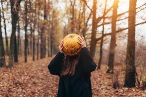 A terrible creature in the autumn forest in the evening. Happy Halloween. Pumpkin head. Man with a pumpkin on his head and a black cloak photo