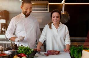 Handsome young African chef is cooking together with his Caucasian girlfriend in the kitchen using red wine as an ingredient. photo