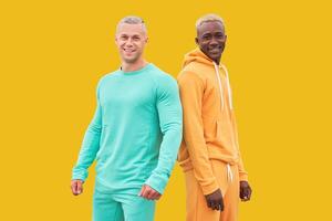 Multi ethnic friends. Two men different color black African-American ethnicity and white Caucasian ethnicity standing isolated yellow background photo