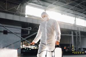 Man dressed white protective overalls spraying surface antibacterial sanitizer sprayer during quarantine photo