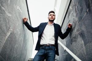 Young stylish businessman man with a beard in a fashionable suit and jeans. Modern image of business youth. It stands on the background of marble walls photo