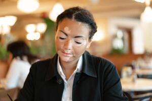 A beautiful young girl of African ethnicity with vitiligo sitting in a restaurant photo