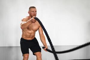 Gym battle rope man stamina training Athlete guy fitness exercising endurance indoor workout. photo