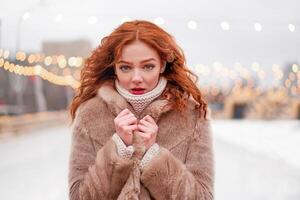 Young beautiful redhead girl freckles ice rink on background. Pretty woman curly hair portrait walking on new year fair photo