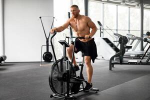 Man exercise bike gym cycling training fitness. Fitness male using air bike cardio workout. photo