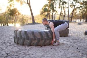 Strong man training workout lifting large tire outdoor DIY gym. photo