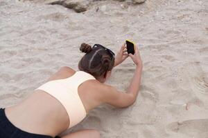 Beautiful woman taking photos on yhe knees with smart phone technology on paradise beach destination summer wanderlust vacation