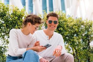 Young modern couple use smartphone sitting bench outdoor in office district. photo