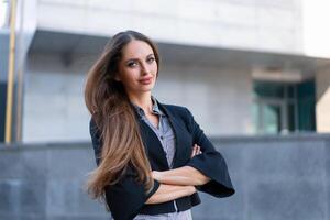 Business woman with long hair dressed black jacket standing outdoor near corporate office building hands folded photo