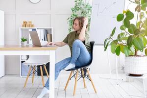 Business woman using laptop sitting desk white modern office interior with houseplant photo