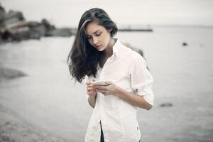 retrato de adolescente niña caminando en el playa es comprobación en línea el móvil teléfono esperando para un mensaje foto