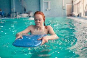 hermosa joven pelirrojo caucásico niña nada en el interior nadando piscina. sano estilo de vida. foto