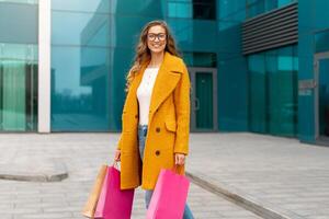 Business woman with shopping bags dressed yellow coat walking outdoors corporative building background photo