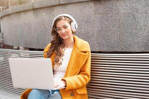 Business Woman Wear Eyeglasses Listen Music Headphone Outdoor Sitting Bench Using Laptop Outdoor photo