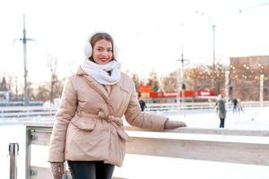 Beautiful lovely young adult woman brunet hair warm winter jackets stands near ice skate rink background Town Square. Christmas mood lifestyle photo