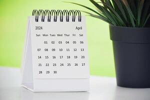 April 2024 desk calendar with potted plant on a desk with green background. photo