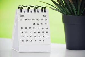 May 2024 desk calendar with potted plant on a desk with green background. photo