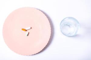 Top view of tablets on a plate next to a glass of water, on a white background. photo