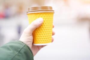 unrecognizable man holding yellow paper cup with coffee outdoors photo