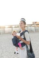 a small child sits in a backpack and walks along with the mother along the seashore. Summer family vacation concept photo