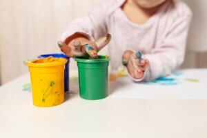 Beautiful little girl draws with finger paints on a white sheet of paper. Creative child development in kindergarten or free time at home photo