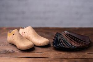 Leather samples for shoes and wooden shoe last on dark wooden table. photo