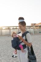 a small child sits in a backpack and walks along with the mother along the seashore. Summer family vacation concept photo