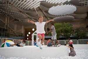 contento pequeño niña jugando blanco el plastico pelotas piscina en diversión parque. patio de recreo para niños. foto