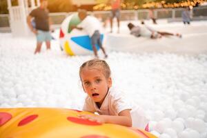 contento pequeño niña jugando blanco el plastico pelotas piscina en diversión parque. patio de recreo para niños. foto