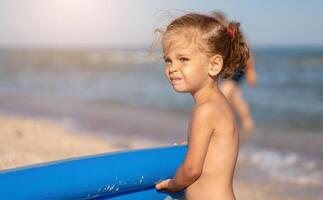 Close up portrait little Caucasian girl on beach skeptical about looking at camera. photo