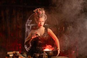 Halloween Witch with cauldron. Beautiful young woman conjuring, making witchcraft photo